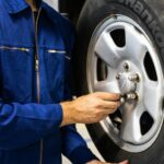 Mechanic in blue coveralls inspecting a car tire in an auto repair workshop.