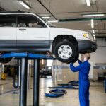 A mechanic inspecting a white SUV lifted in a well-lit auto repair shop.